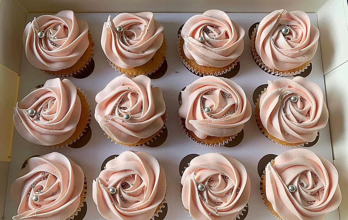 Row of cupcakes with pink rose-shaped frosting on a white tray.