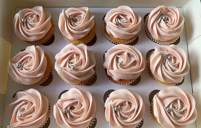 Row of cupcakes with pink rose-shaped frosting on a white tray.